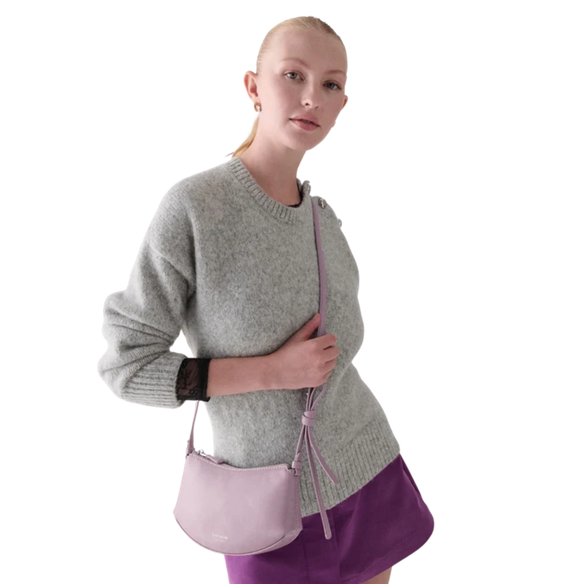 Modelo luciendo un bolso crossbody cuero brillante en color violeta con un suéter gris y falda morada.